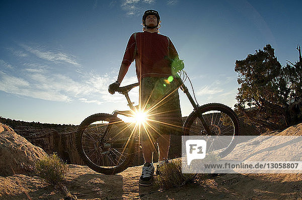 Low angle view of man with bicycle standing on mountain against sky