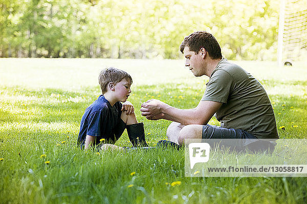 Seitenansicht von Vater und Sohn auf einem Grasfeld im Park sitzend