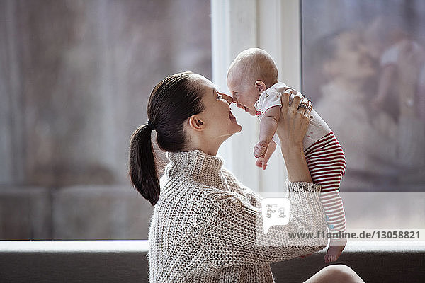 Seitenansicht einer glücklichen Frau  die zu Hause mit einem kleinen Mädchen die Nase reibt