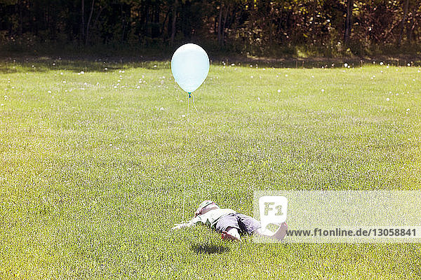 Auf Grasfeld liegender Junge mit Ballon