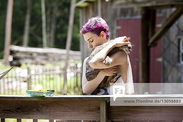 Frau umarmt Katze  während sie am Geländer steht