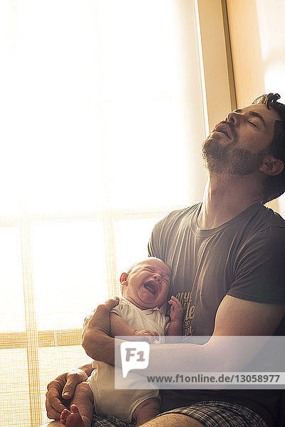 Frustrierter Vater hält weinendes Baby zu Hause gegen Fenster