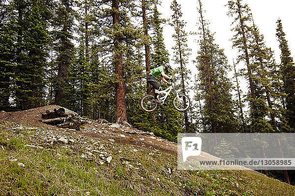 Seitenansicht eines Radfahrers  der beim Radfahren im Wald einen Stunt macht