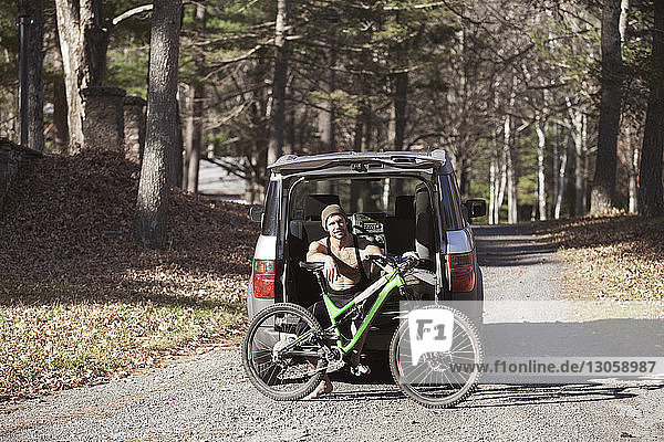 Porträt eines Mannes mit Mountainbike auf Kofferraum eines Autos sitzend