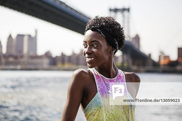 Lächelnde Frau steht am Fluss vor der Manhattan-Brücke