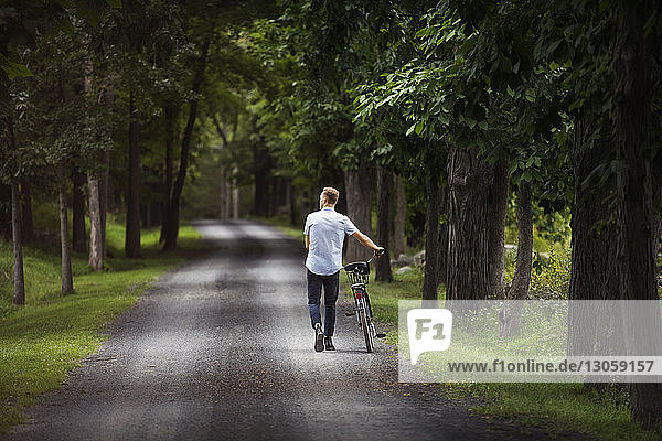 Man walking on road with bicycle in forest