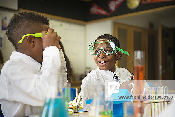 Glücklicher Junge trägt eine Schutzbrille  während er einen Freund im Labor ansieht