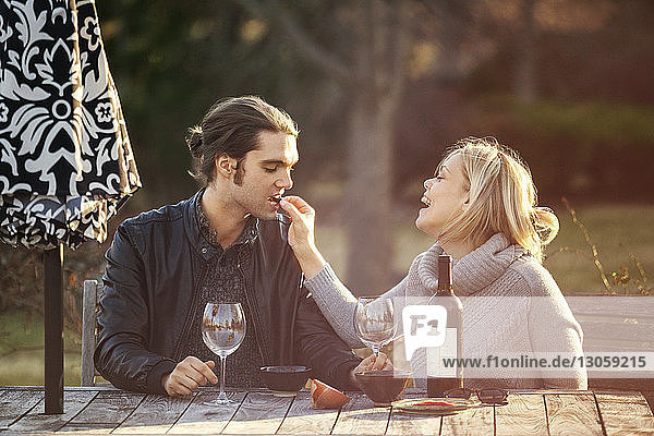 Fröhliche Frau füttert Mann am Picknicktisch im Park