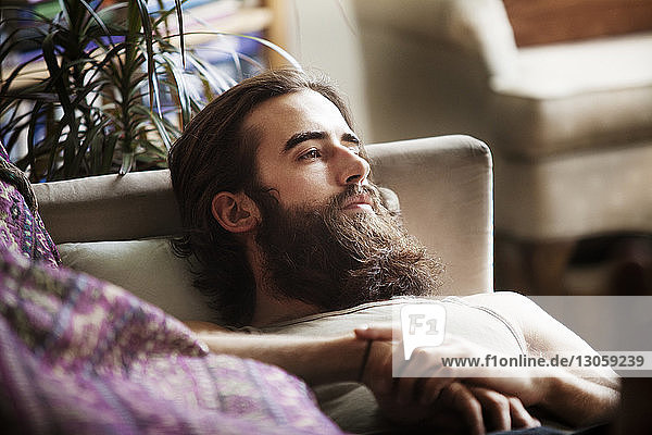 High angle view of thoughtful man relaxing on sofa