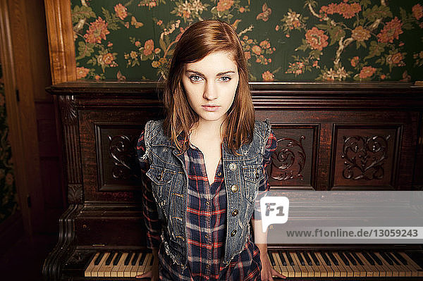 Portrait of young woman standing against piano at home