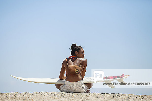 Rear view of woman with surfboard sitting at beach