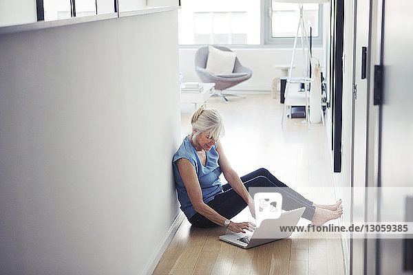 Ältere Frau sitzt auf dem Boden und benutzt zu Hause einen Laptop