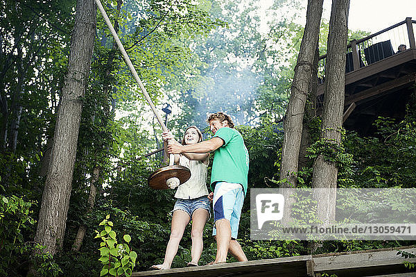 Low angle view of happy couple holding rope swing in forest