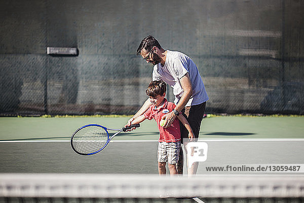 Vater unterrichtet Sohn Tennis auf dem Platz