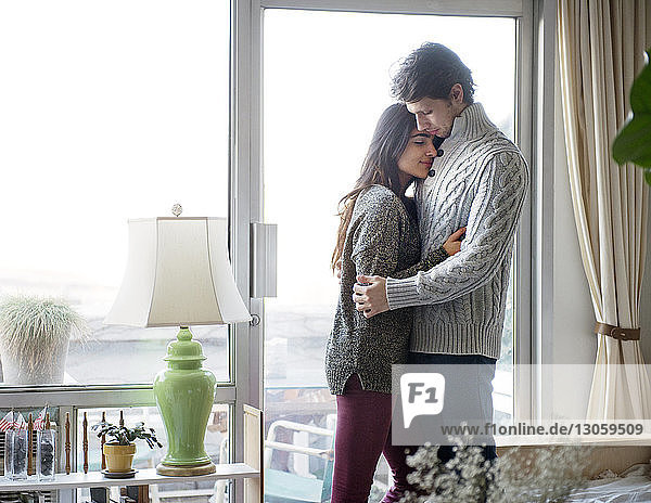 Young couple embracing against window at home