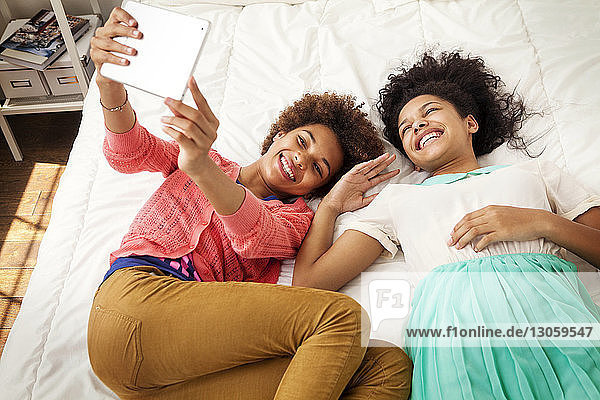High angle view of siblings photographing while lying on bed at home