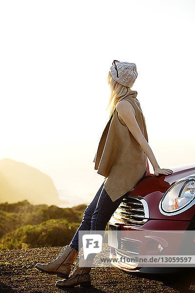 Seitenansicht einer Frau  die sich auf dem Feld gegen den klaren Himmel am sonnigen Tag an ein Auto lehnt