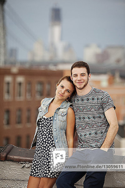 Portrait of young couple standing on building terrace against city