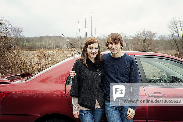 Portrait of happy young couple standing against car