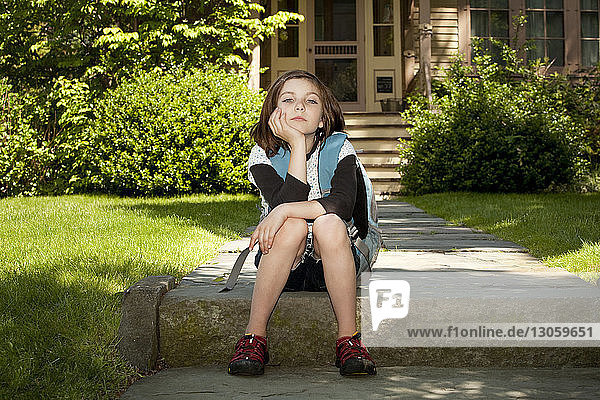 Portrait of girl with backpack sitting on footpath