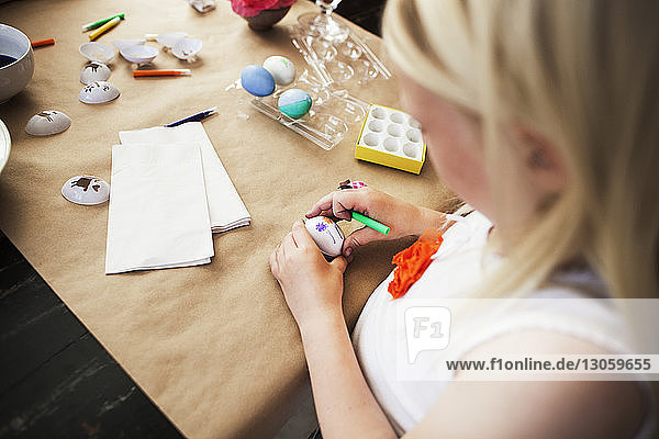High angle view of girl decorating Easter egg on table at home