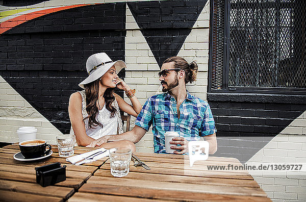 Young couple talking while sitting by table at sidewalk cafe
