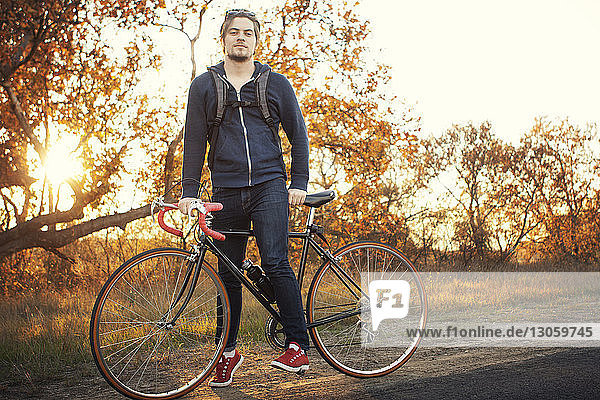 Portrait of man standing with bicycle on road during sunset