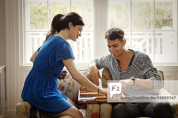 Couple playing Backgammon while sitting on armchair at home