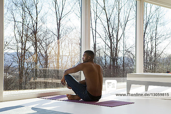 Rear view of man sitting on exercise mat at home
