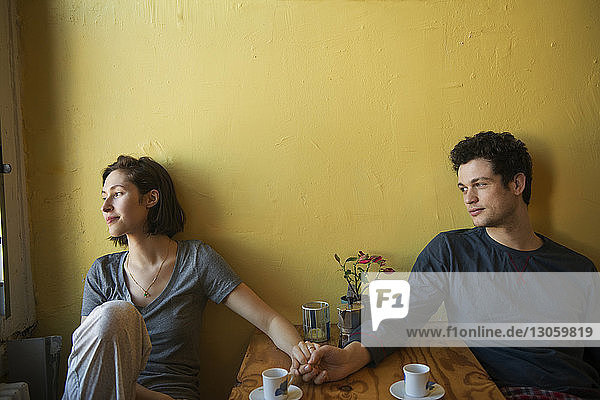 Lächelndes Paar hält Hände auf dem Tisch gegen die Wand