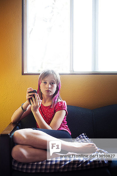 Portrait of girl using mobile phone while sitting on sofa at home