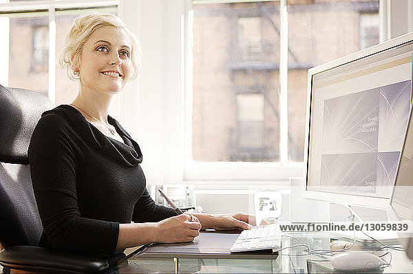 Lächelnde Geschäftsfrau benutzt Computer auf dem Tisch im Büro