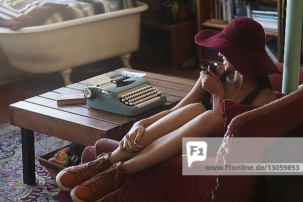 Happy woman drinking coffee while sitting by typewriter at home