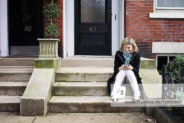 Woman using smart phone while sitting on steps outside house