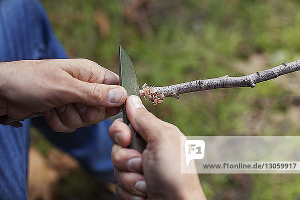 Beschnittenes Bild eines Mannes  der im Wald einen Stock mit einem Messer schneidet