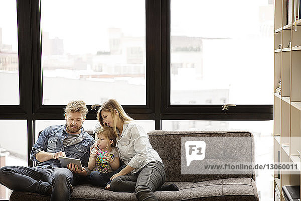 Familie benutzt Tablet-Computer  während sie zu Hause auf dem Sofa sitzt