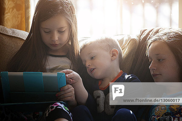 Siblings looking at tablet while sitting on sofa at home