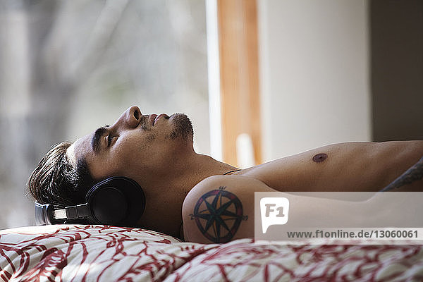 Side view of man listening music while lying on bed at home