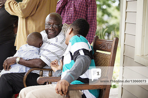Glücklicher älterer Mann sitzt mit Enkeln auf der Veranda