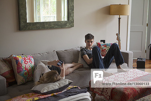 Boy looking at sister using mobile phone while lying on sofa