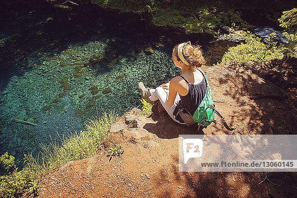 High angle view of female hiker sitting on rock against lake