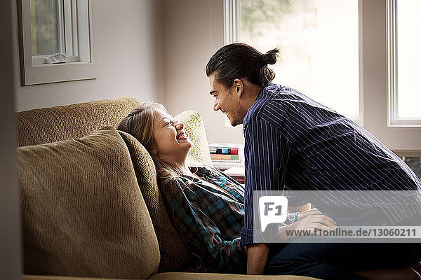 Cheerful couple looking at each other while sitting on sofa