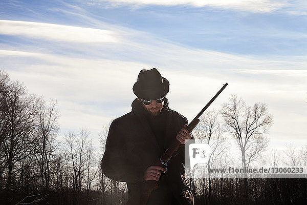 Man holding rifle while standing against sky