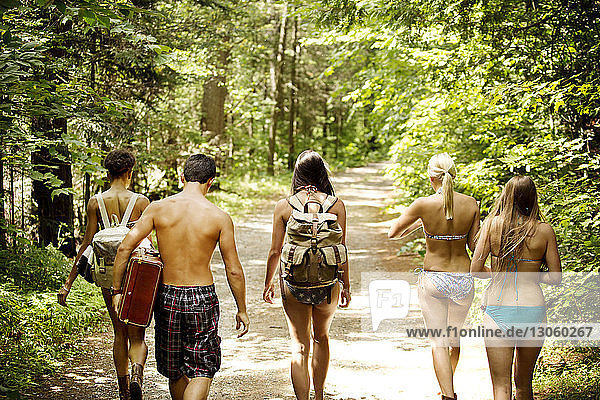 Rear view of friends walking on road amidst trees