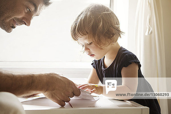 Close-up of father teaching daughter coloring at table in home