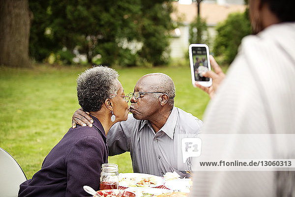 Cropped image of woman photographing senior couple kissing in backyard