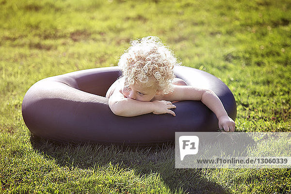Boy lying amidst black inflatable ring on grassy field