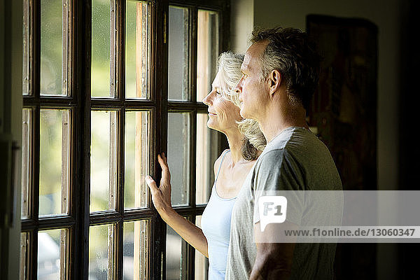 Nachdenkliches älteres Ehepaar schaut durch das Fenster  während es zu Hause steht