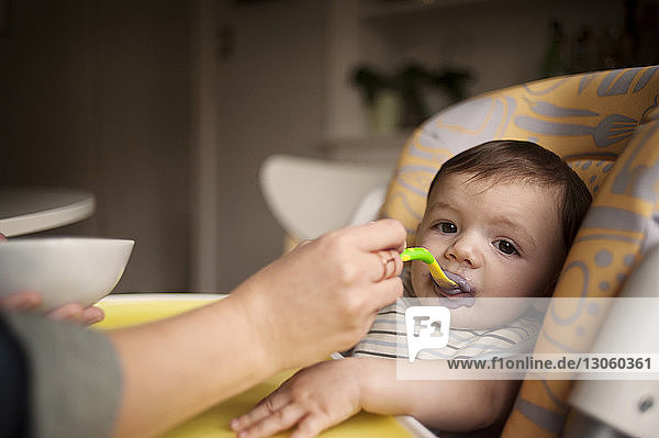 Ausgeschnittenes Bild einer Mutter  die ihren kleinen Jungen zu Hause von Hand füttert