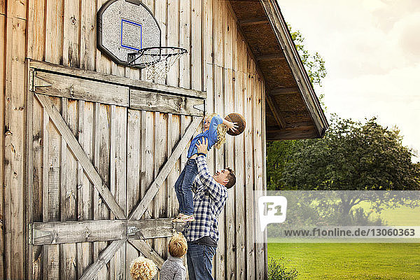 Glücklicher Vater trägt Tochter  während er mit Kindern Basketball spielt